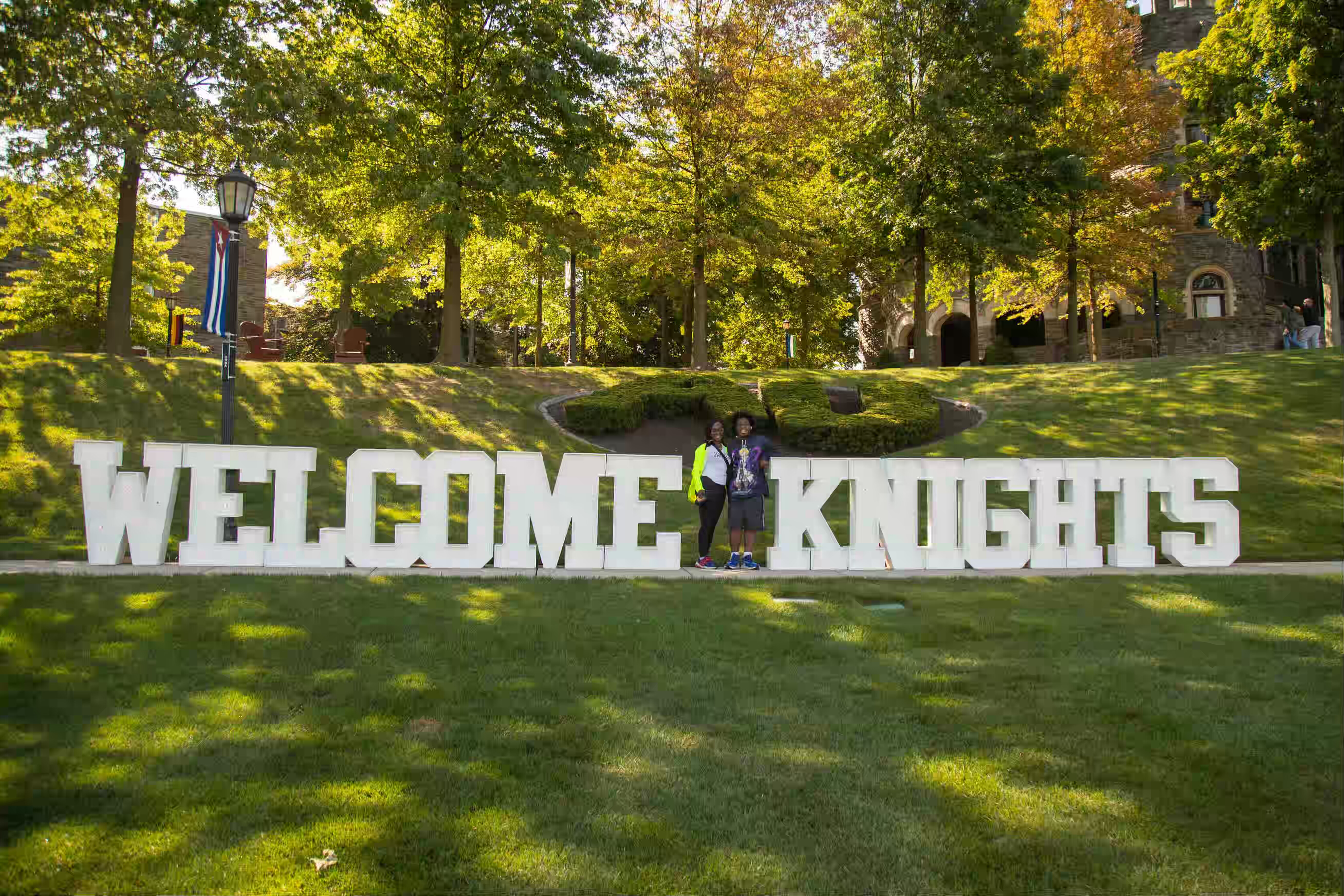 Proud parent and student pose in front of 'Welcome Knights' sign on move-in day