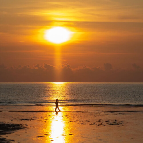 A person walking on the beach during a sunset.