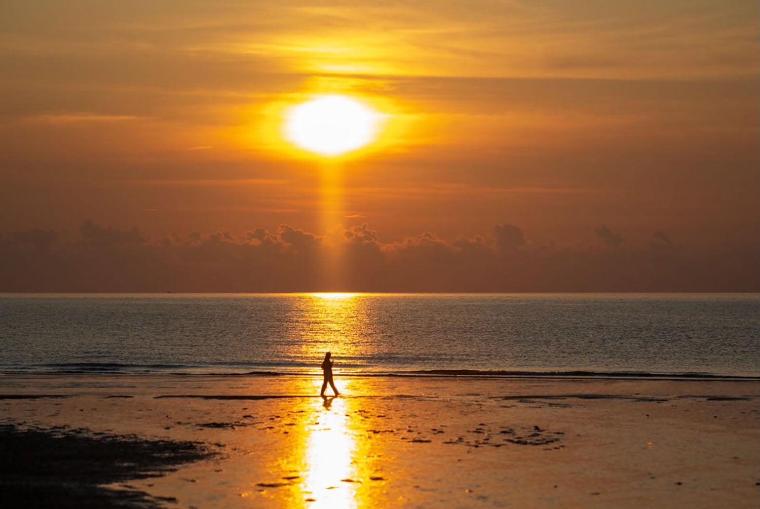 A person walking on the beach during a sunset.