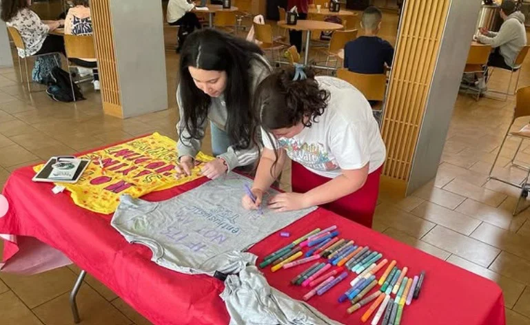 Two students seated at a table, collaborating on designing t-shirts during an event.