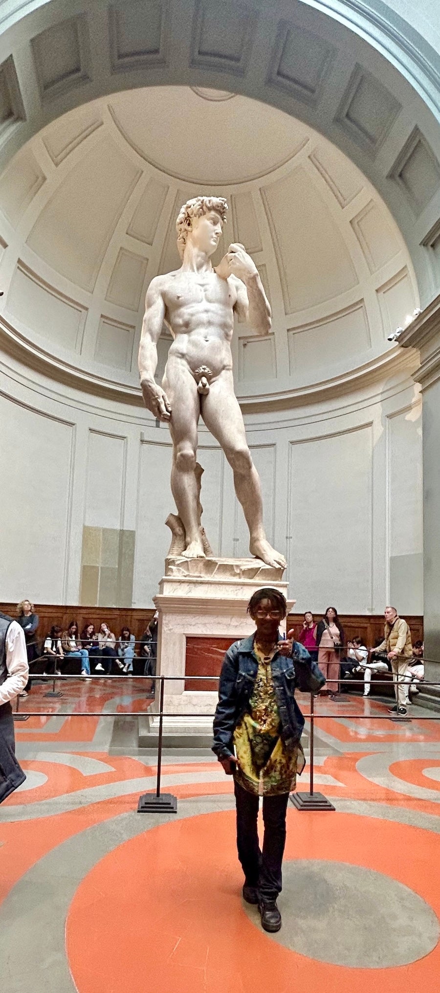 A student stands in front of the David statue in Florence, Italy, giving a thumbs up