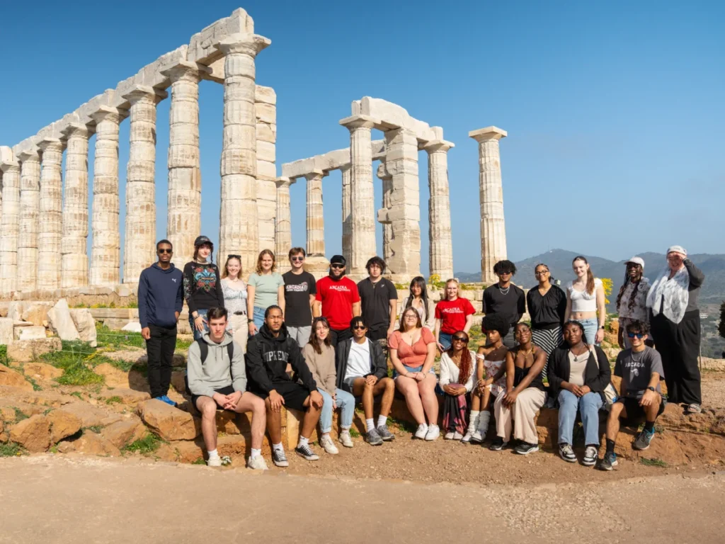 A class of preview students poses outside near ancient architecture in Greece.