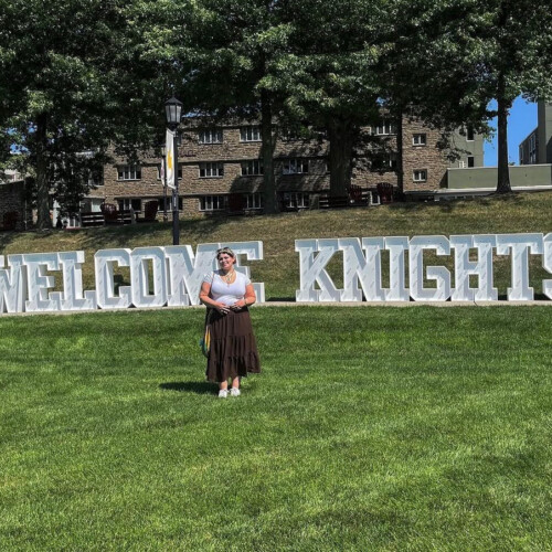 JJ Demetrius ’26 standing in front of the "Welcome Knights" sign on Haber Green.