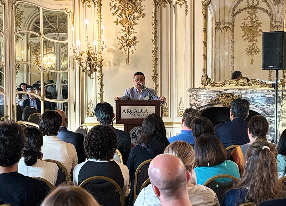 Dr. Raghu Kurthakoti stands at a podium delivering welcome remarks