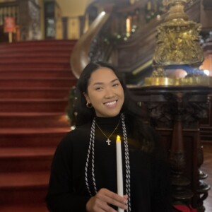 Karen Hua '26M holds a candle and stands in front of the Grand Staircase in Grey Towers Castle