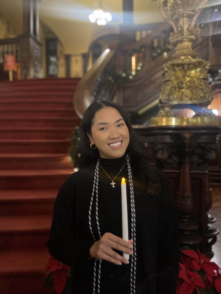 Karen Hua '26M holds a candle and stands in front of the Grand Staircase in Grey Towers Castle