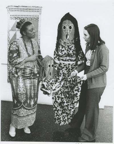 A black and white photo of two women holding a patterned dress.
