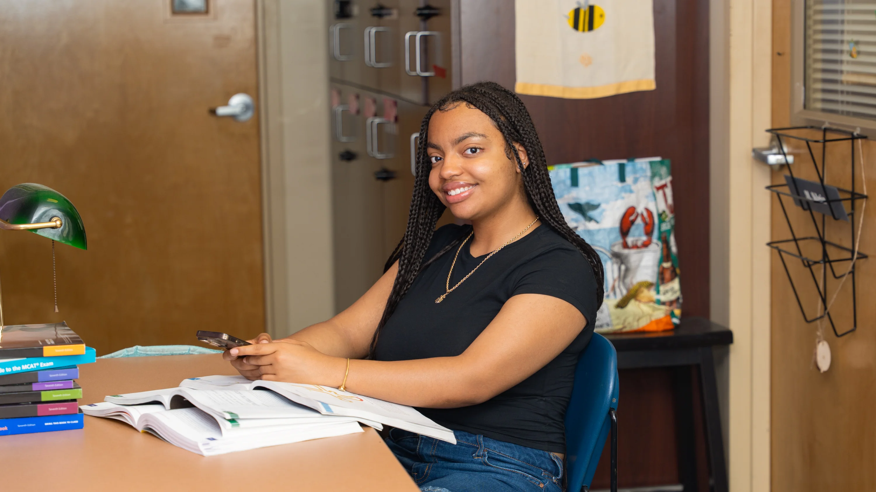 A student sits at a desk with textbooks and smiles towards the viewer in the Hive.