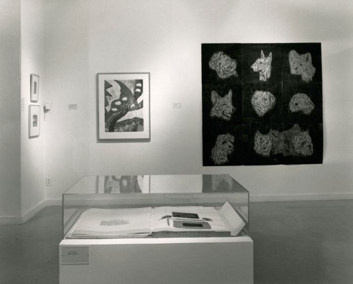 Photo of an exhibit with a book in a glass case and a painting with dogs in the back.