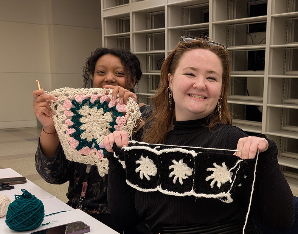 Raine Robinson ’24, ’26MPH and a friend pose with their crocheting projects at the Central Parkway Library in Philadelphia.