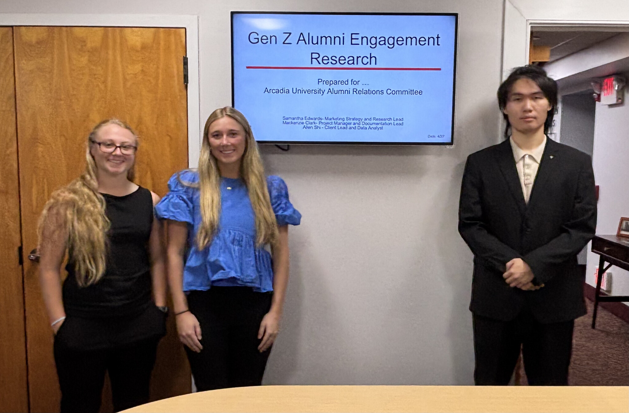 Mackenzie Clark ’27, Samantha Edwards ’27, Allen Shi ’26 stand in front of their powerpoint presentation.