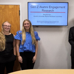 Mackenzie Clark ’27, Samantha Edwards ’27, Allen Shi ’26 stand in front of their powerpoint presentation.