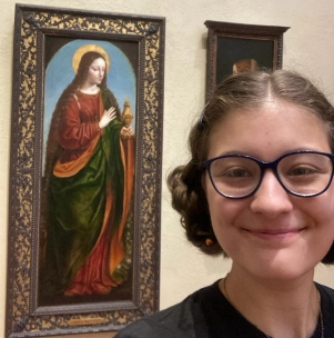 Honors Convocation 2025 award recipient Abigail Emory takes a selfie in front of a painting.