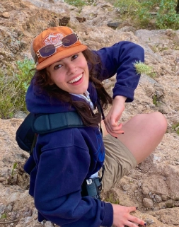 Honors Convocation 2025 award recipient Delaney Grace Aikins sits on a small cliff and smiles at the camera behind her.