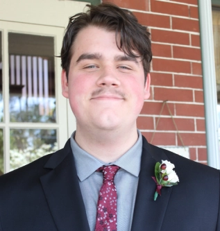 Honors Convocation 2025 award recipient Kieran Barber smiles in front of a white door with red brick surrounding it.
