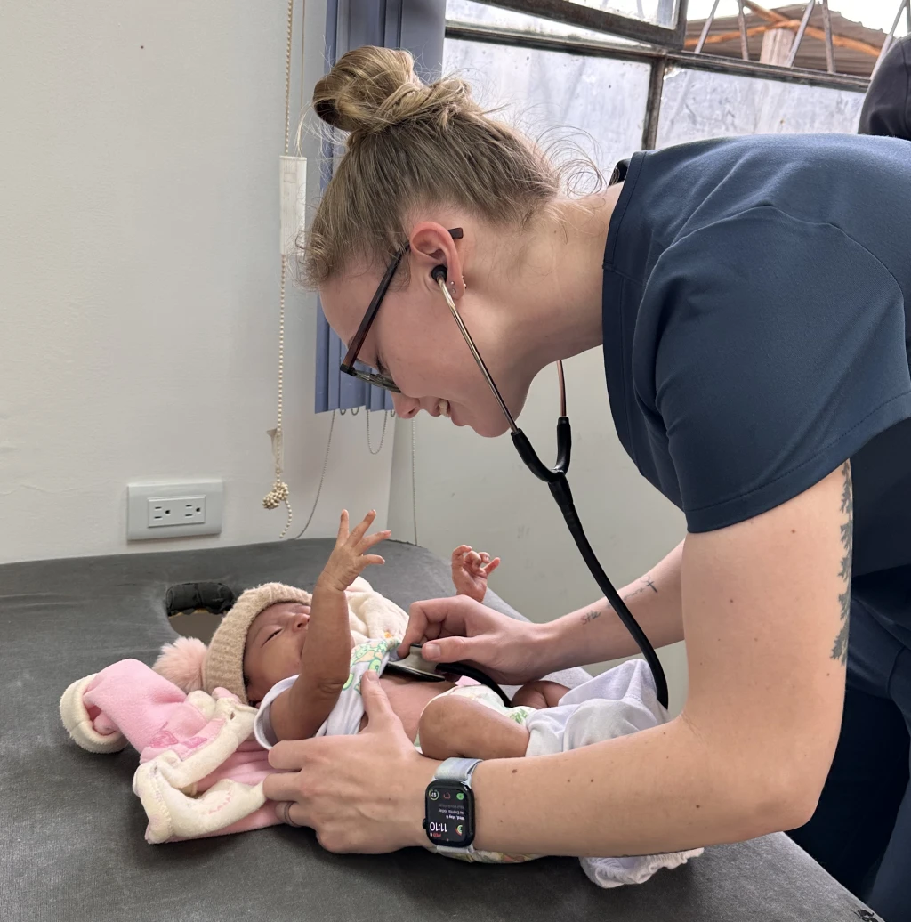 A woman measures an infant's heartrate using a stethoscope.