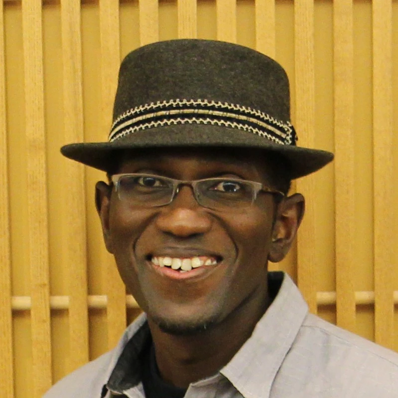 Alex Otieno wears a hat in a portrait headshot.
