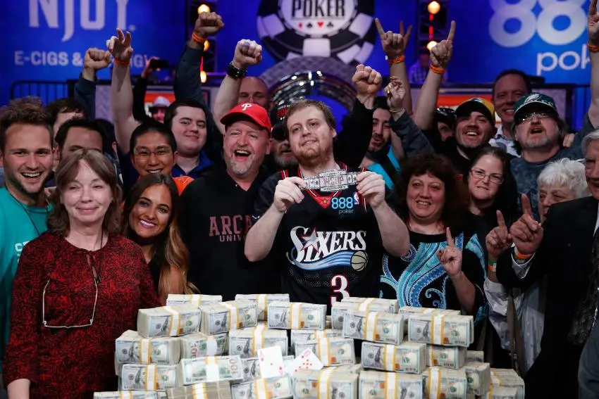 A group of people posing with a person who just won a competition with a pile of cash in front of them.
