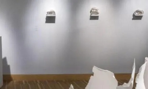 A mostly empty art gallery with the exception of a pillar containing three white dishes stacked on top of each other