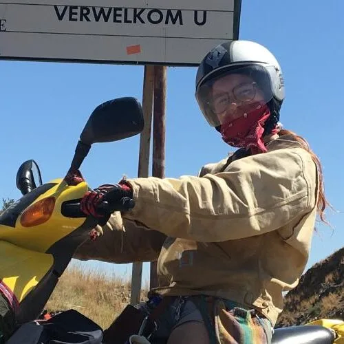 A student on a yellow motorcycle, wearing a helmet and a bandana to cover the mouth