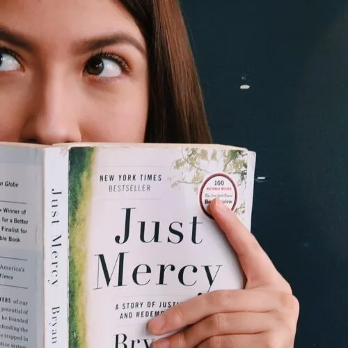 A woman hiding her face with a book named "Just Mercy".