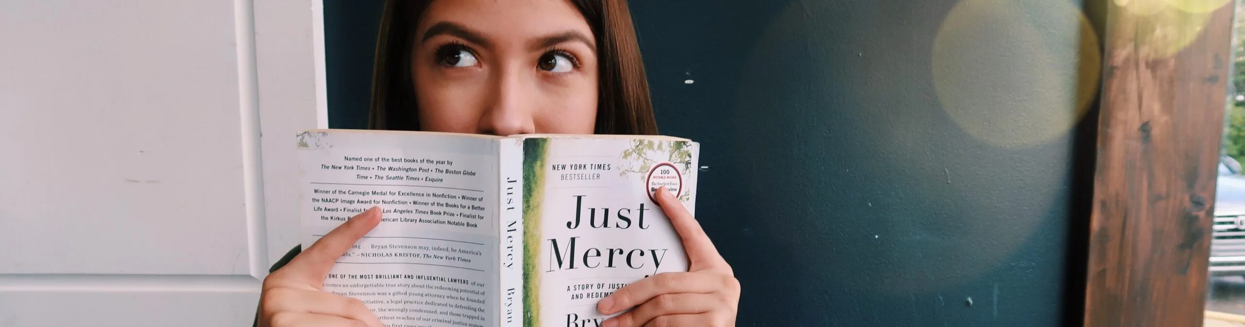 A woman hiding her face with a book named "Just Mercy".