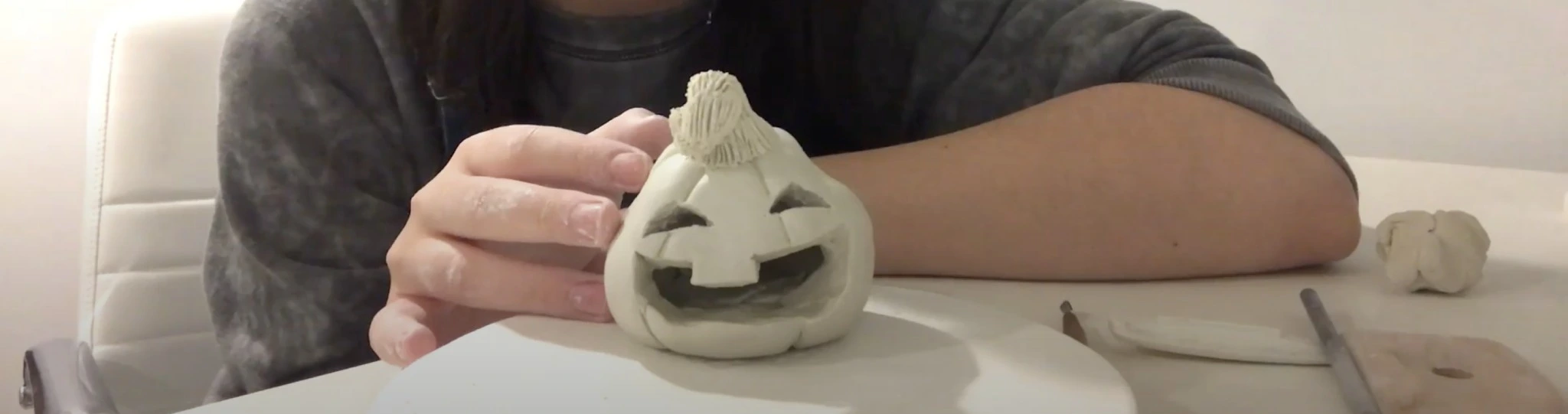 Someone making a ceramic jack-o-lantern pumpkin.