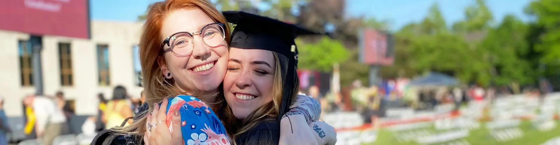 Student in cap and gown hugging friend