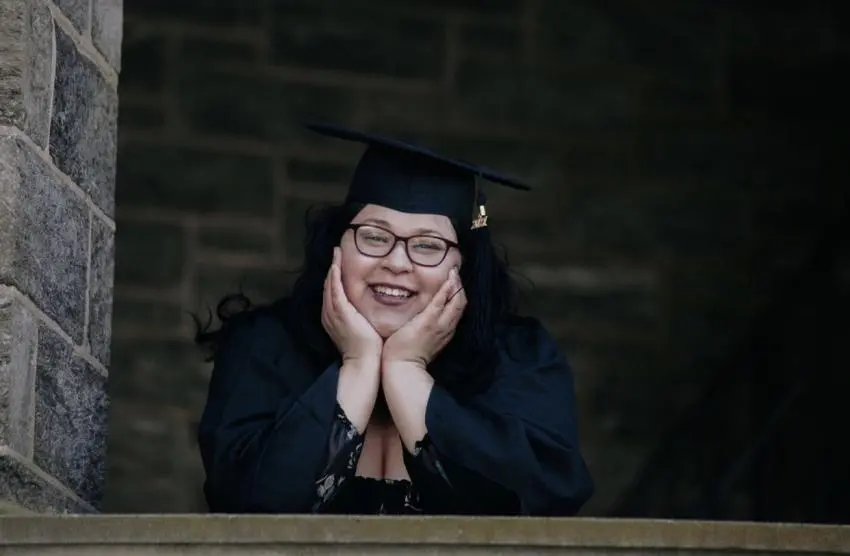 A portrait of a graduate holding their face outside of Grey Towers Castle.