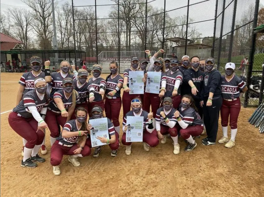 Women's softball team posing for a picture, holding up signs and wearing green bands.