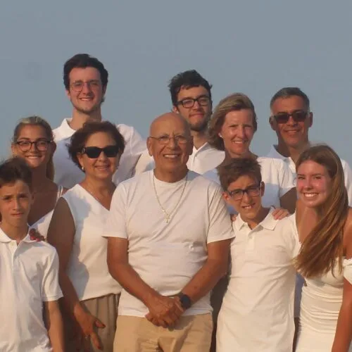 Group photo consisting of 24 people where white or off white on a beach.