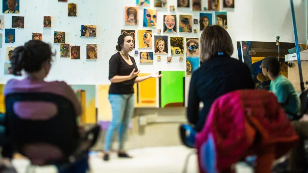A student points to artwork in studio during class discussion.