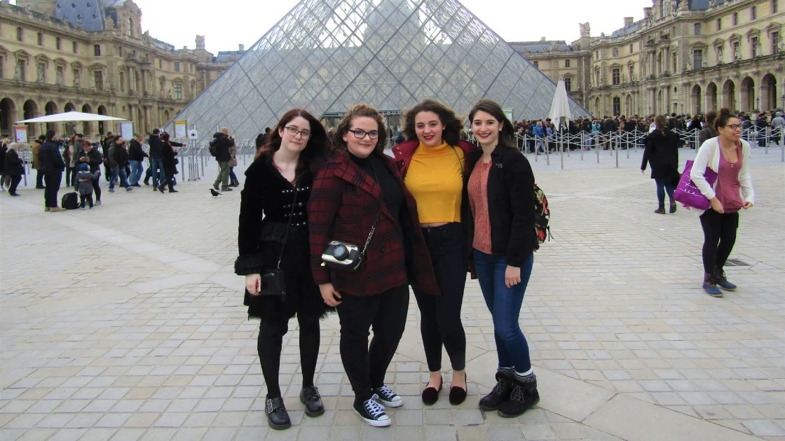 Four Arcadia students stand in front of the pyramid entrance of the Louvre in Paris, France as they study abroad.