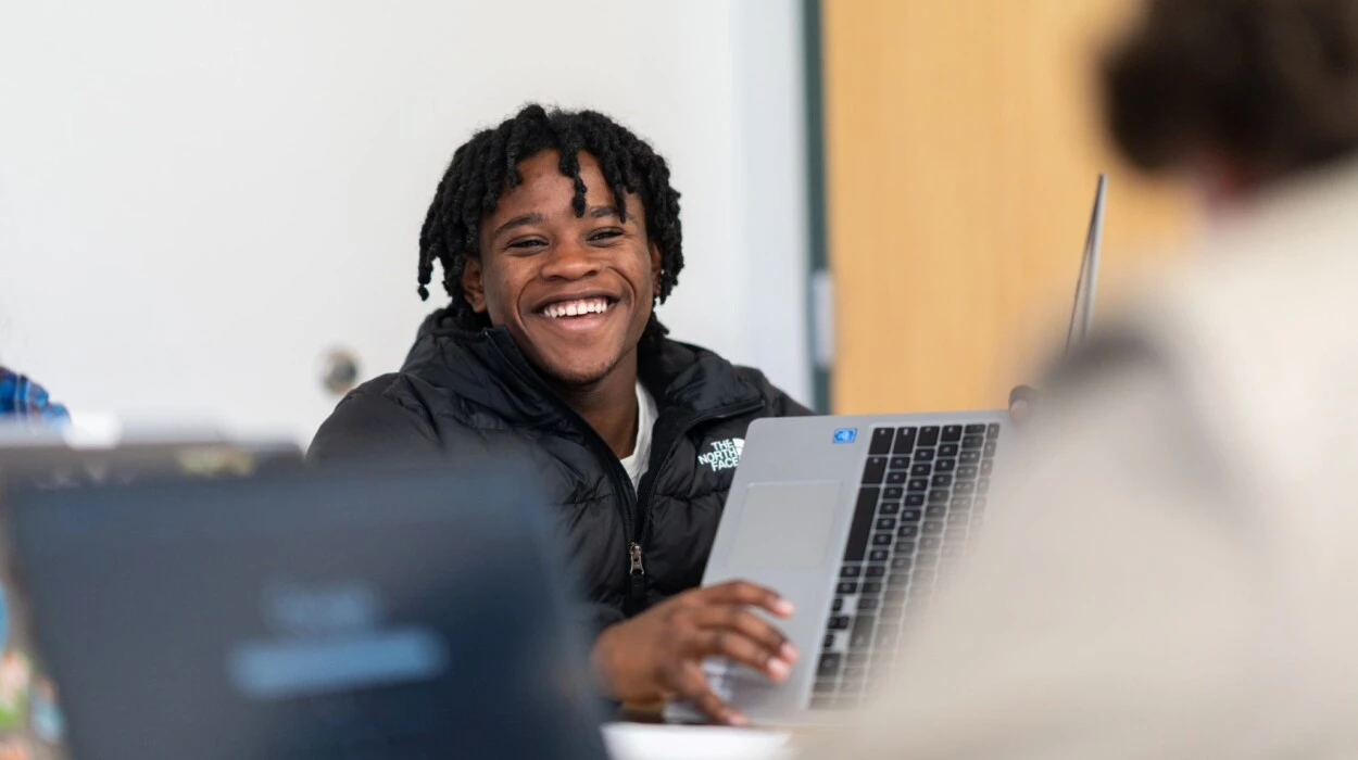 A student smiles and holds up his computer