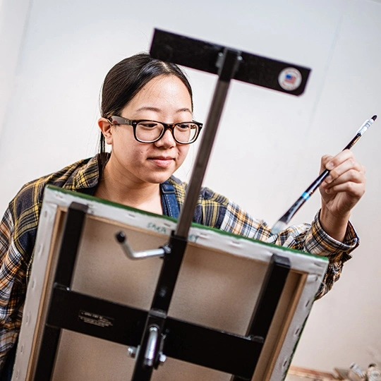 An Arcadia University student paints on a canvas.