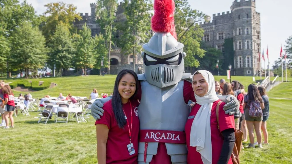 The Arcadia Knight mascot with two students, smiling and looking towards the camera.