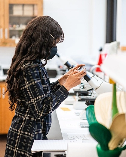 An undergraduate student using a microscope in lab class.