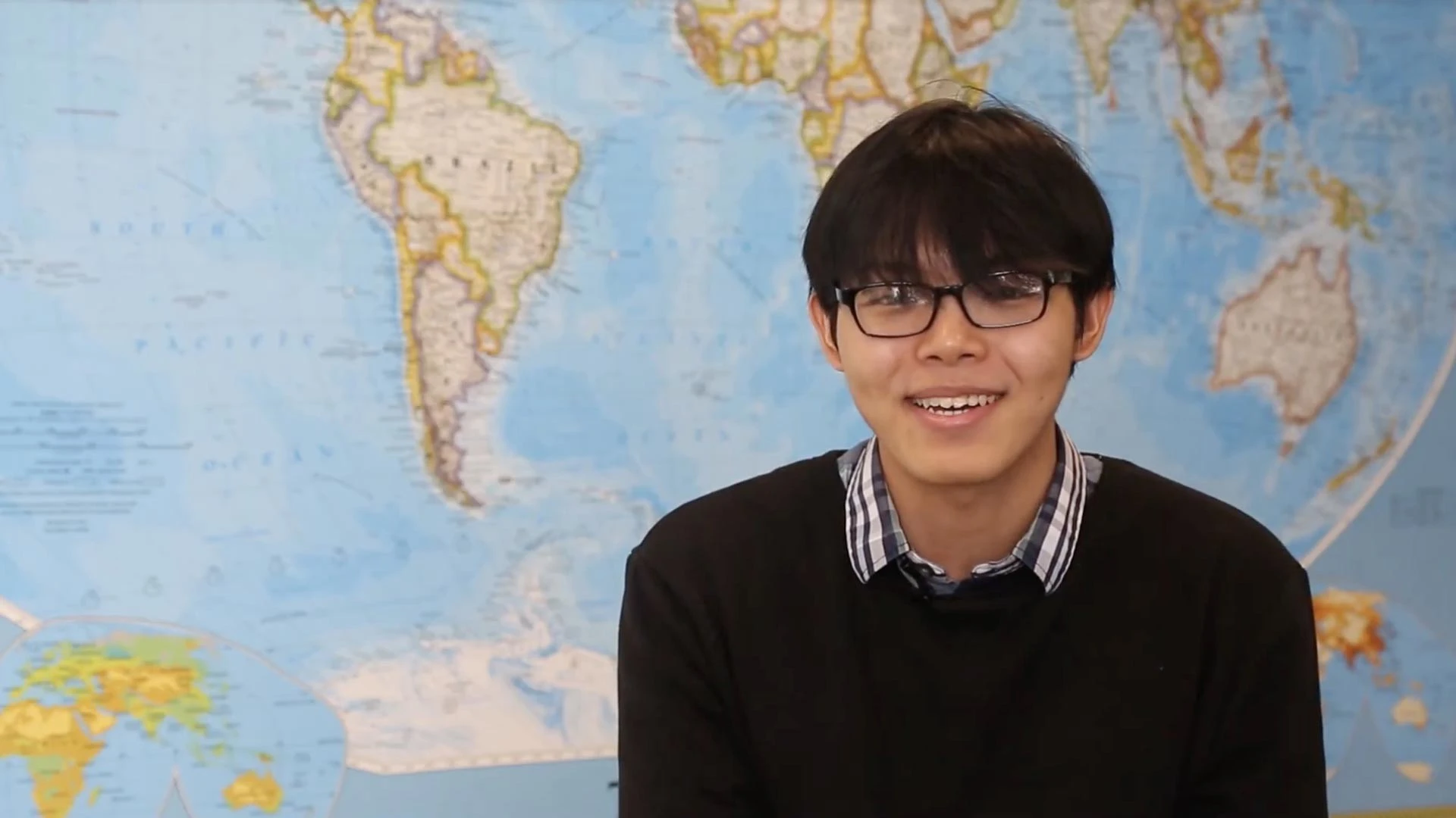 Student smiling and sitting in front of world map.