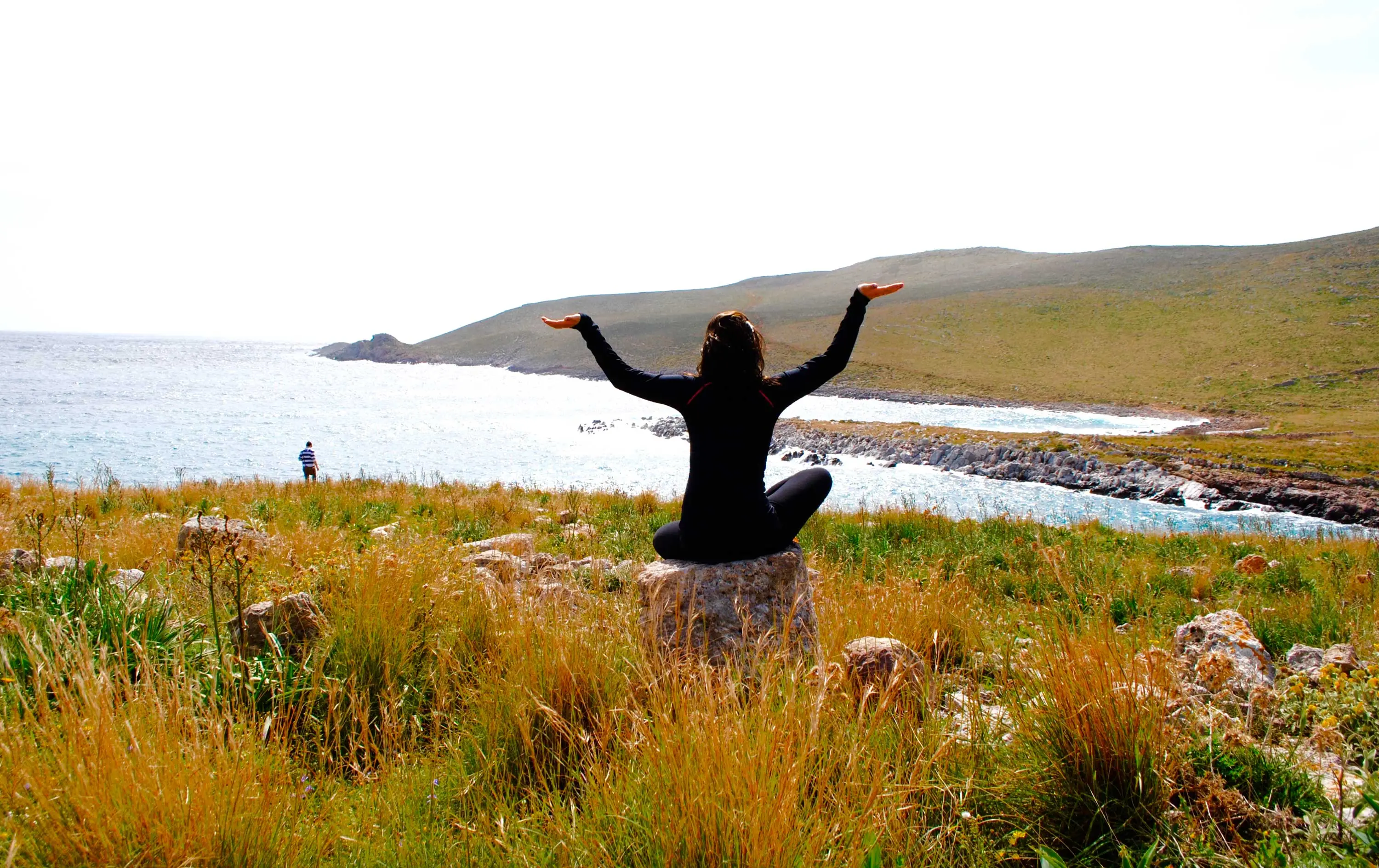 Student sides cross legged on rock while staring at the ocean in the background.