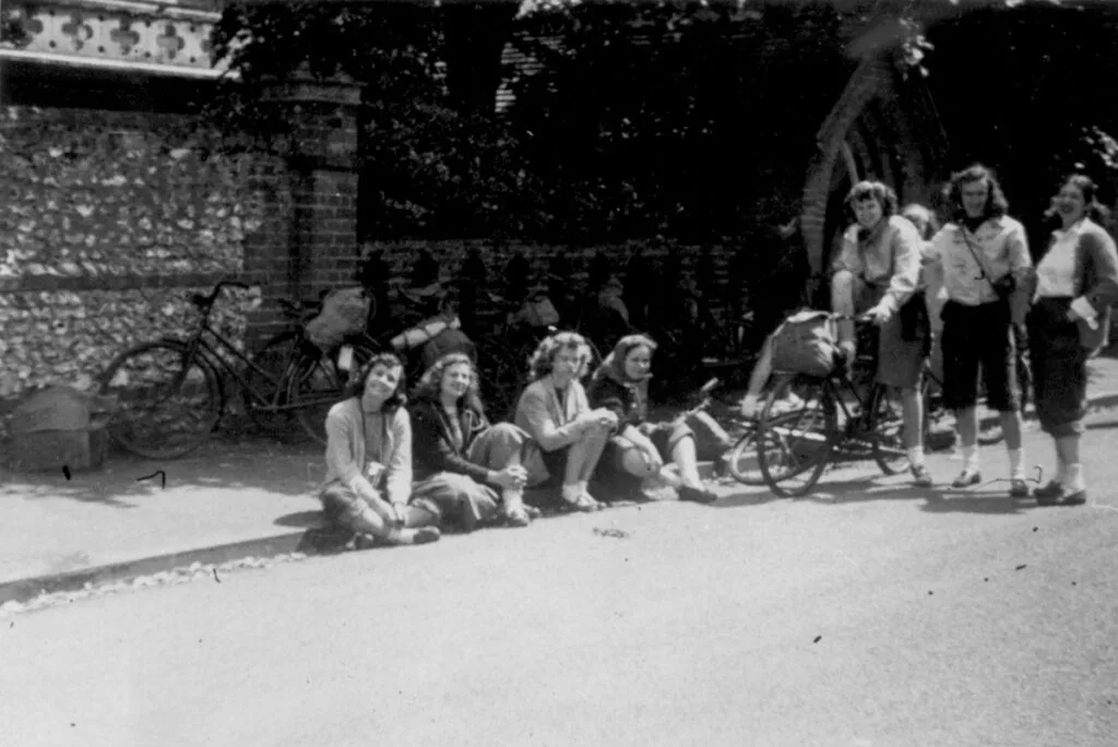 Black and white photo from the 1940s of women sitting on sidewalk and riding bikes