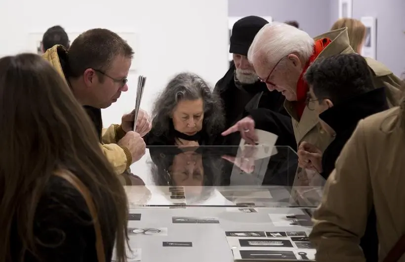 People gather at an art opening and look at artwork under glass case.