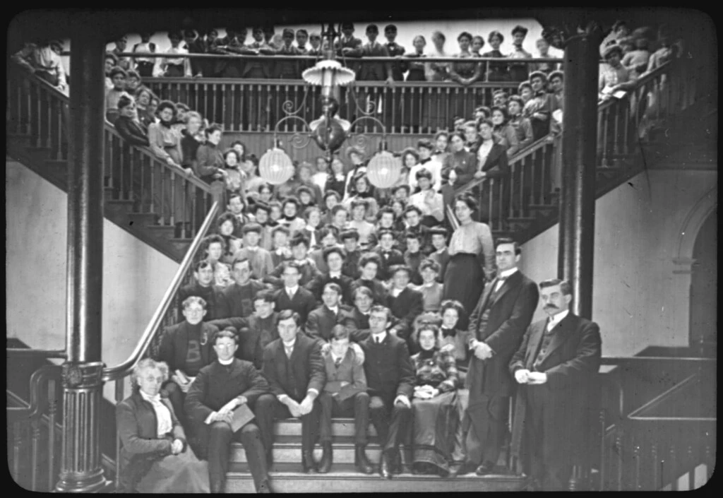 Black and white photo from 1901 of a large group sitting on flights of stairs
