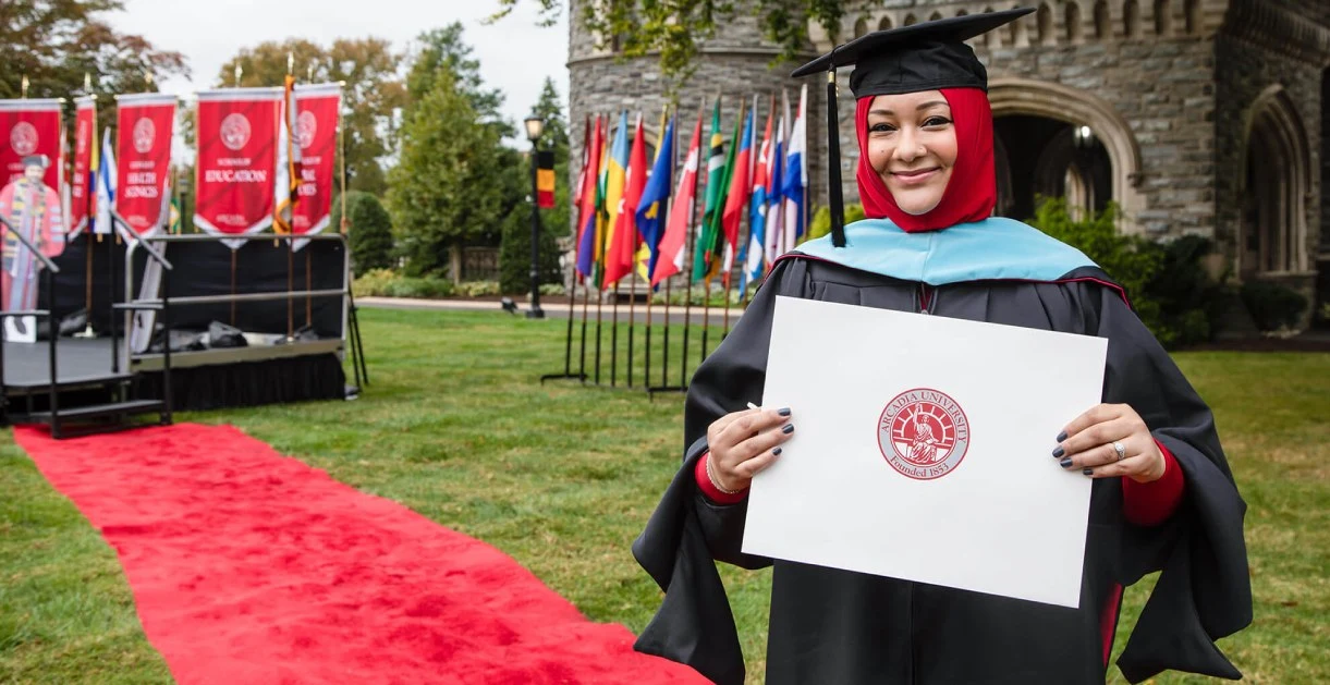 An international student in graduation cap and gown, holding diploma during commencement.