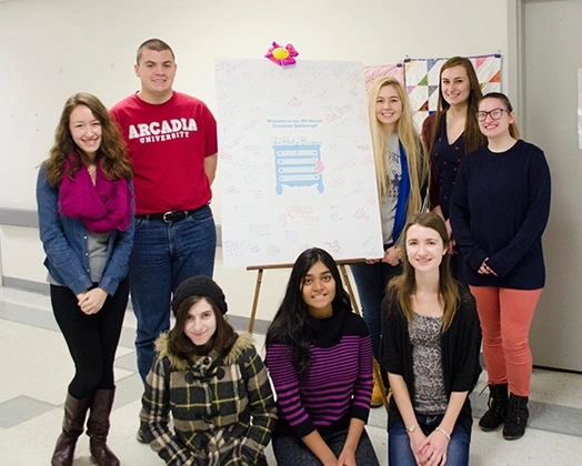 Students stand around easel with information on community outreach program