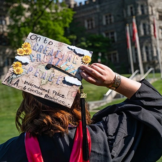 An IPCR student holds a sign at graduation about creating creative peace.