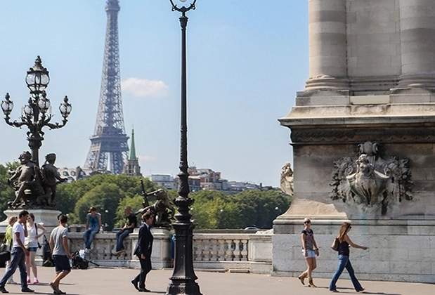 People walking on sidewalk with the Eiffel Tower in the background.