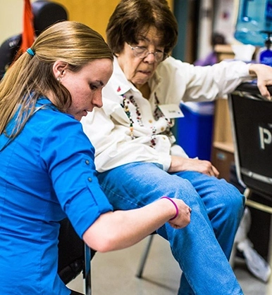 A physical therapy student helps an older adult with her leg.