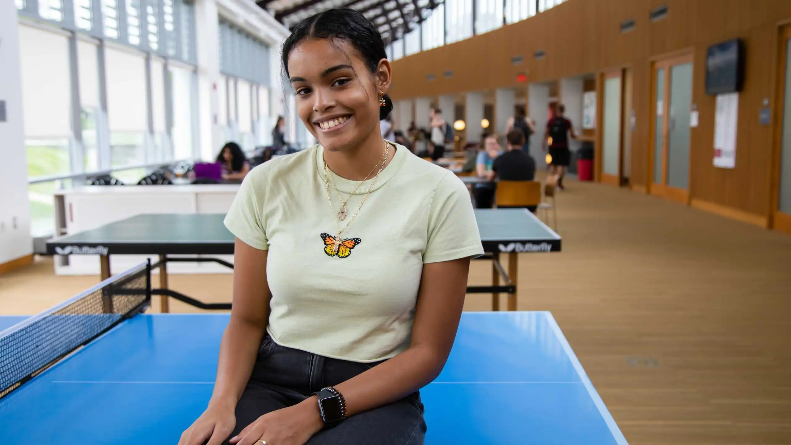 Student smiles at the camera while sitting on a ping pong table