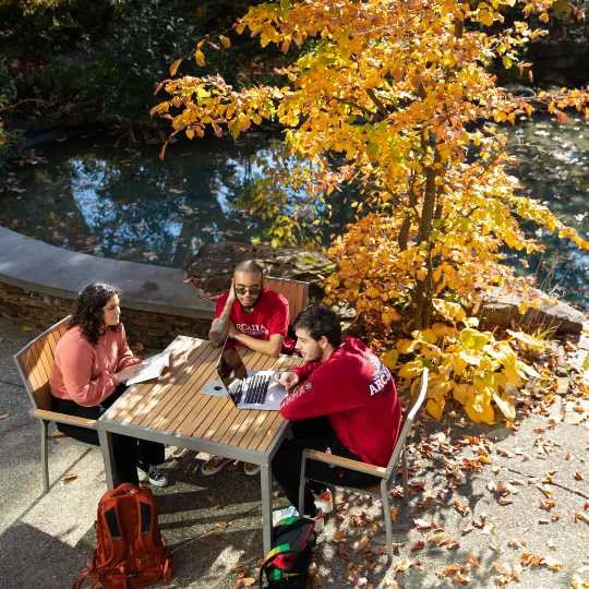 Three students sitting at a table outsides working.