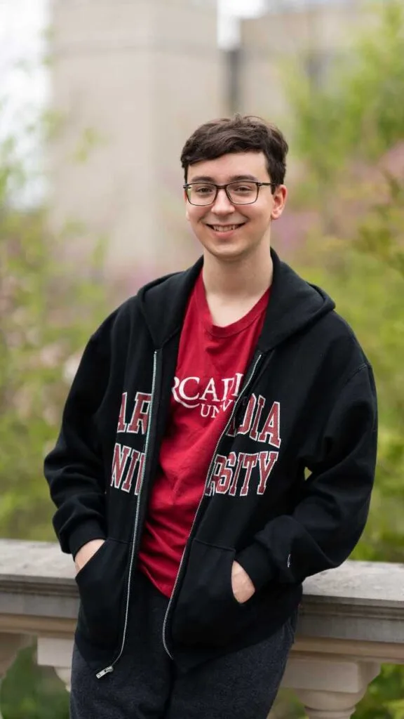 Students smiles at the camera while leaning against railing and wearing an Arcadia shirt and sweatshirt.